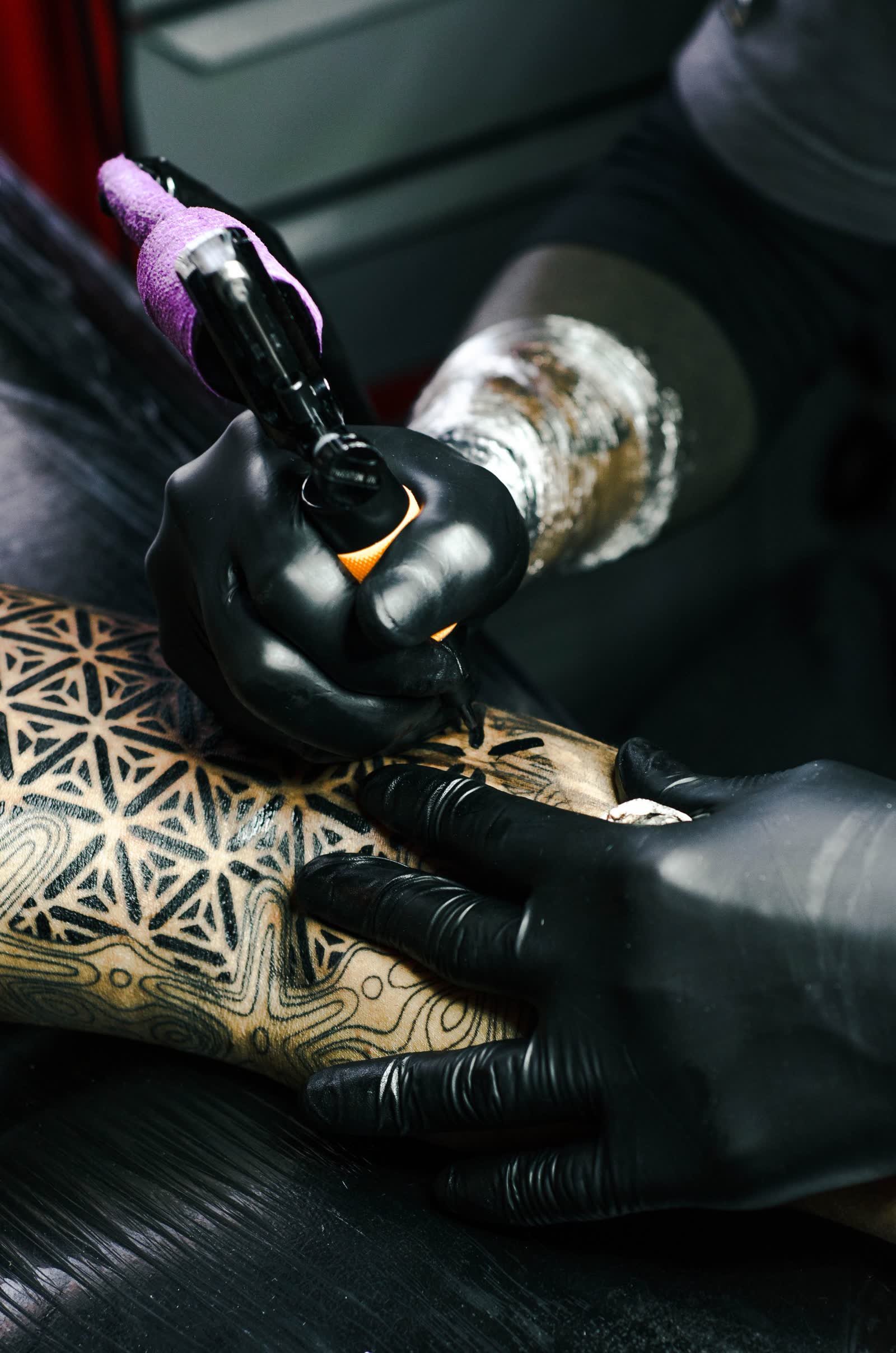 Luvas pretas segurando máquina de tatuagem